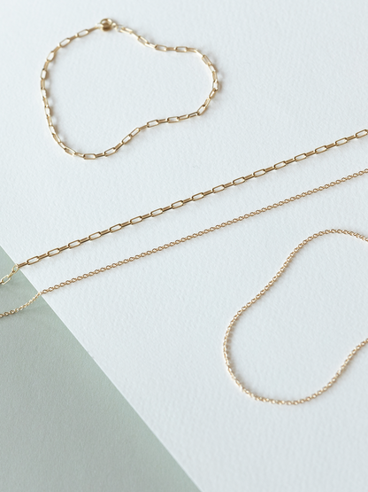 Mini links & cable chain solid gold bracelets & necklaces on a white & grey background