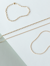 Mini links & cable chain solid gold bracelets & necklaces on a white & grey background