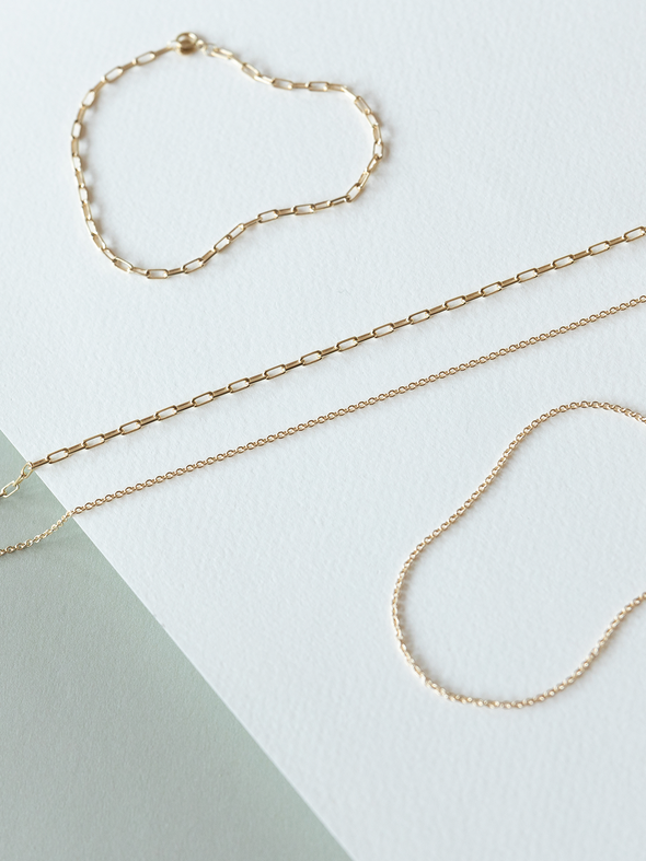 Mini links & cable chain solid gold bracelets & necklaces on a white & grey background