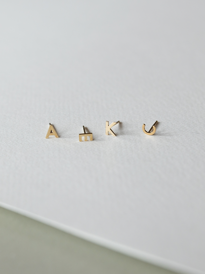 Set of solid gold letter earrings on a light gray background