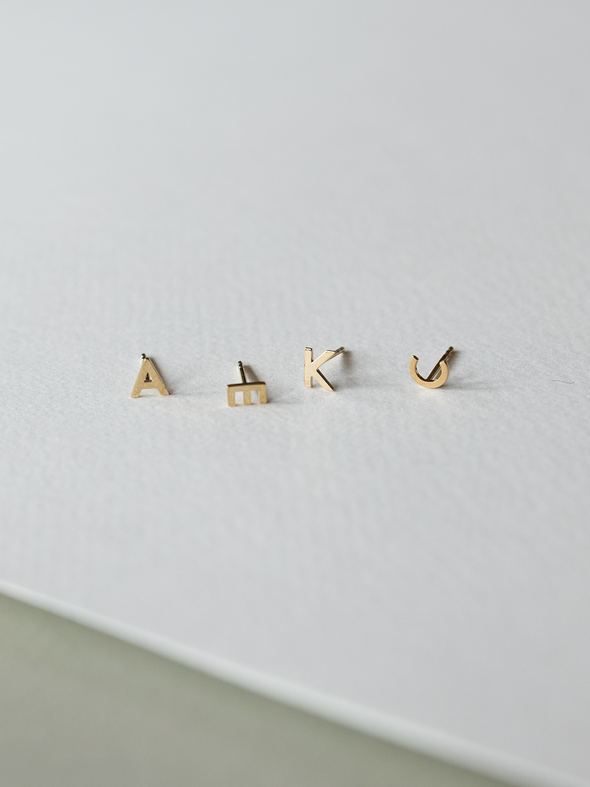 Set of solid gold letter earrings on a light gray background