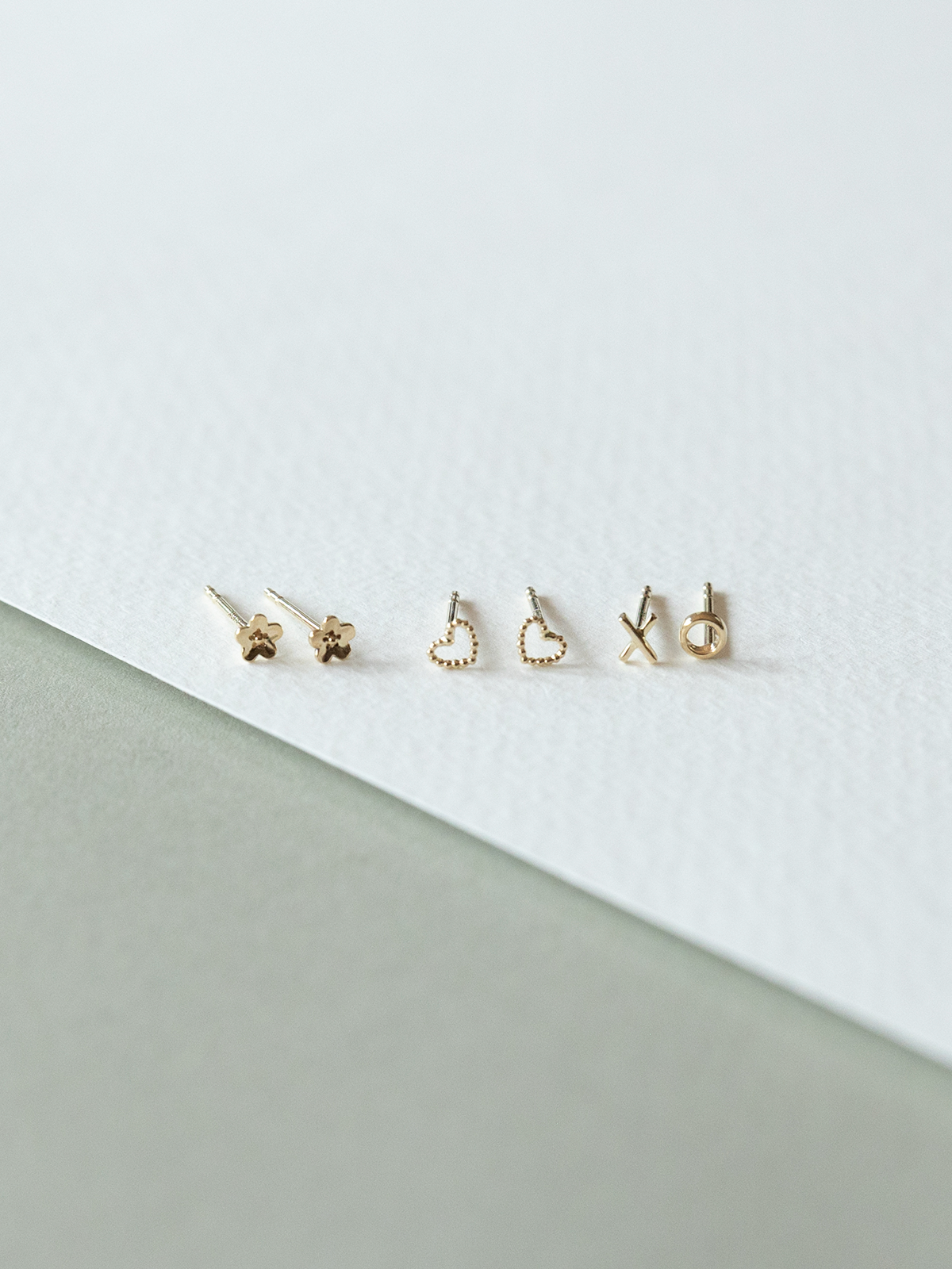 Set of solid gold micro stud earrings on a white and gray background