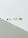 Set of solid gold micro stud earrings on a white and gray background
