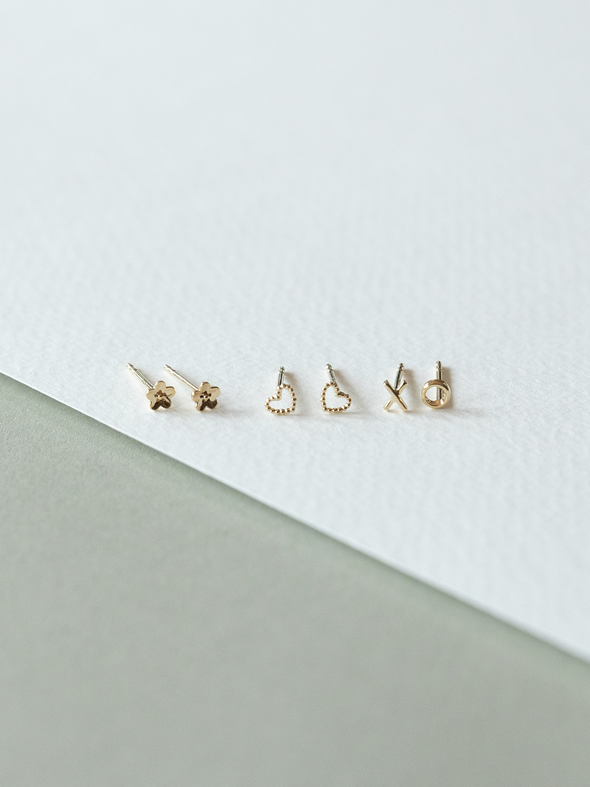 Set of solid gold micro stud earrings on a white and gray background