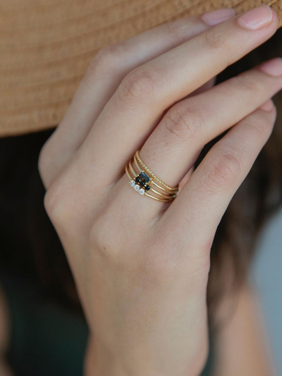 Close-up of a hand wearing a gold ring stack, blurred background