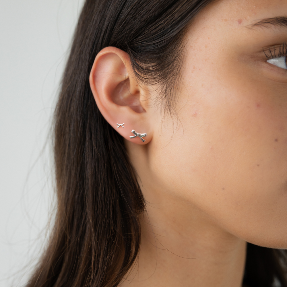 Close-up of a woman wearing silver bow-shaped earrings against a neutral background