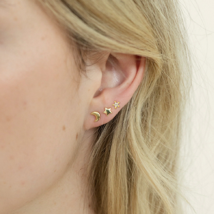 Close-up of an ear wearing gold earrings with a star and moon design.